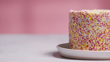 studio shot of paper confetti falling on birthday cake covered with hundreds and thousands decorations