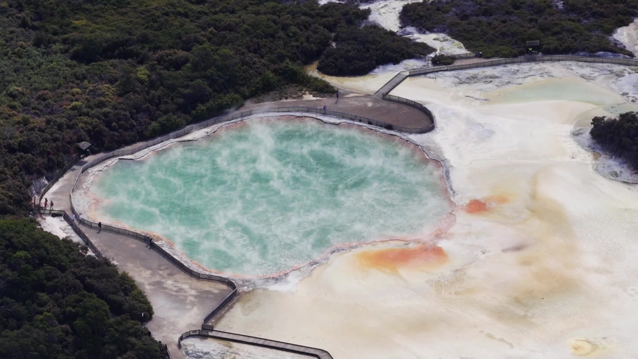 Letecký pohled na živý tyrkysový geotermální bazén obklopený bledými minerálními terasami a oranžovými usazeninami poblíž Rotorua, Nový Zéland, představující pozoruhodnou sopečnou krajinu Severního ostrova