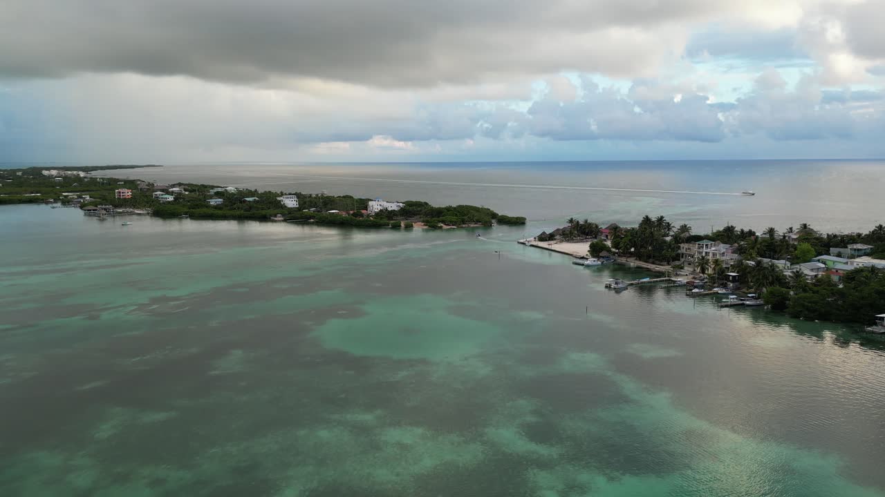 vista de avión no tripulado en belice volando sobre el mar azul oscuro y claro del caribe, un cay de arena blanca cubierto de palmeras y restaurantes en un día nublado