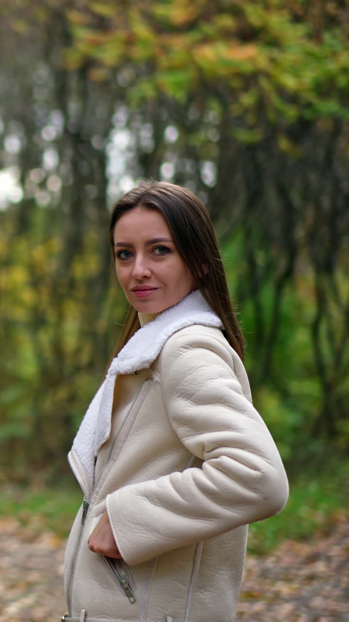 Happy smiling lady with dark long hair standing in the nature. Caucasian woman turns and waves her hair in front of camera in autumn wood. Vertical video