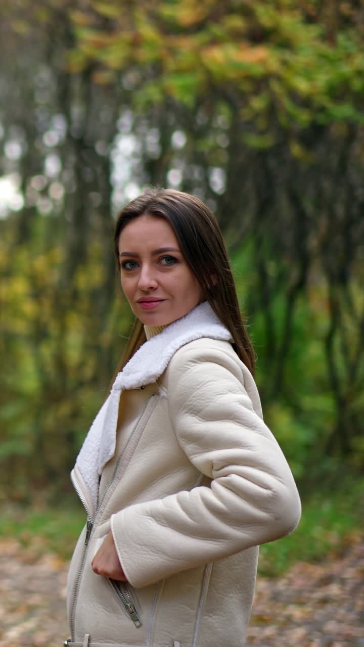 Happy smiling lady with dark long hair standing in the nature. Caucasian woman turns and waves her hair in front of camera in autumn wood. Vertical video