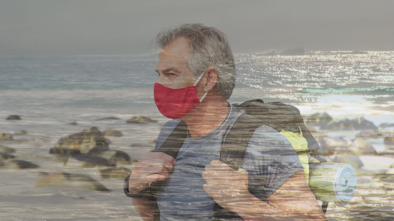 hombre mayor caucásico feliz con máscara facial caminando por la costa sobre las olas del mar