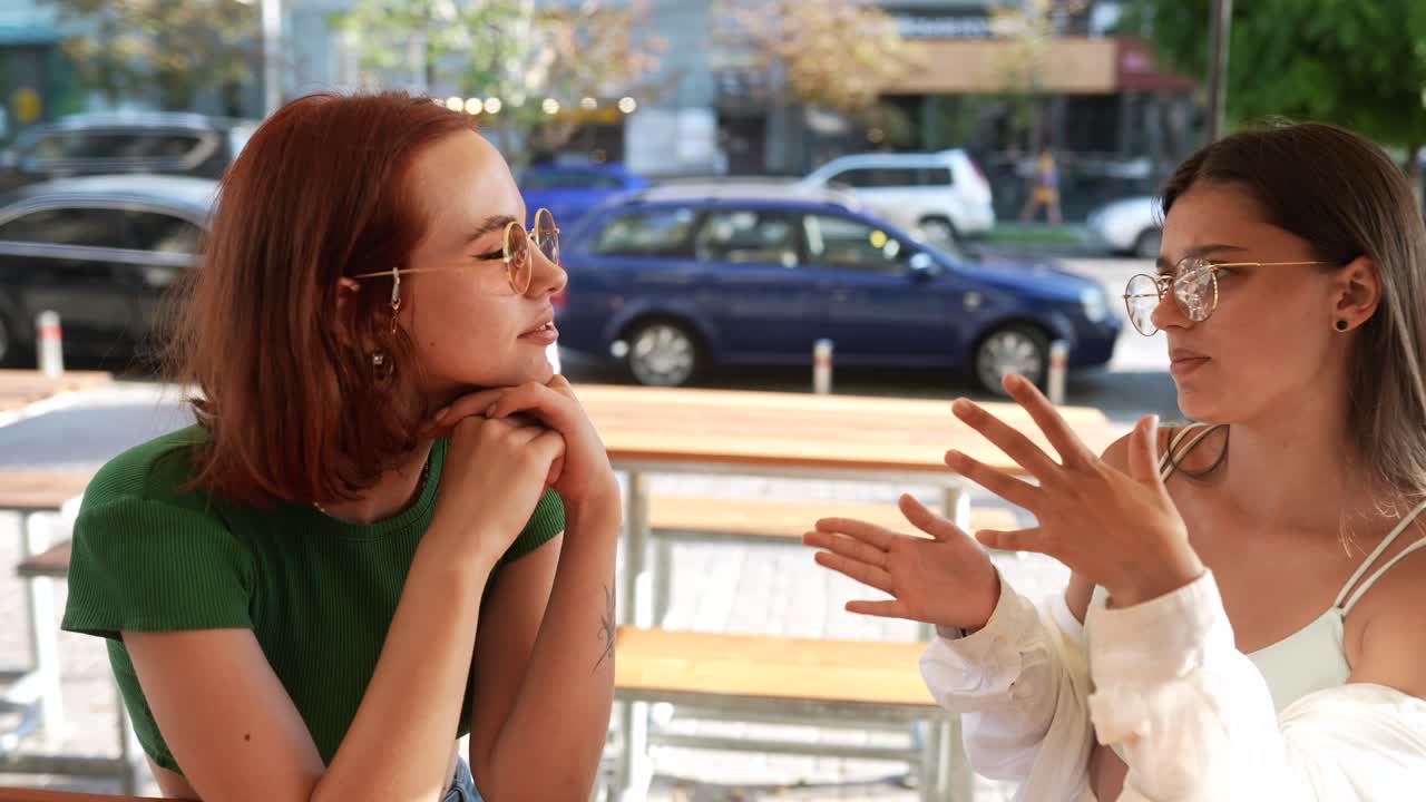dos mujeres jóvenes teniendo una conversación en un café al aire libre