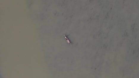 Aerial-Top-Down-View-Of-Lone-Fisherman-On-Traditional-Wooden-Boat-On-River