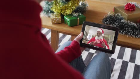 Caucasian-man-waving-and-using-tablet-for-christmas-video-call-with-smiling-santa-on-screen