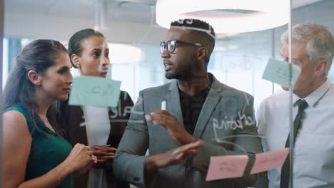 diverse business people using sticky notes african american team leader man brainstorming with colleagues working on solution discussing strategy writing on glass whiteboard in office meeting 4k