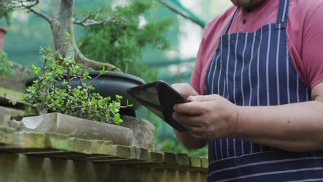 sección media de un jardinero caucásico usando una tableta en el centro del jardín