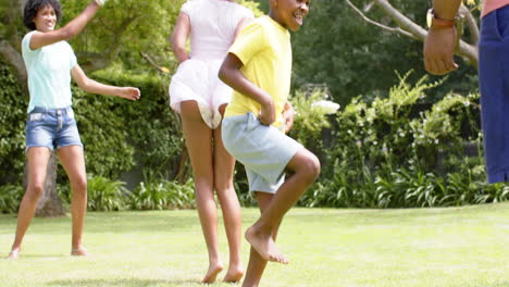 Felices-Padres-Afroamericanos,-Hijo-E-Hija-Saltando-En-Un-Jardín-Soleado,-Cámara-Lenta