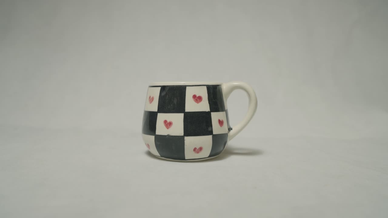 A beautifully painted ceramic mug featuring black and white squares with red hearts.