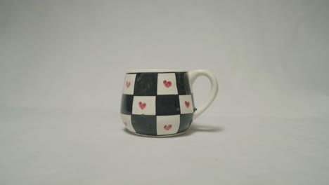 a beautifully painted ceramic mug featuring black and white squares with red hearts.