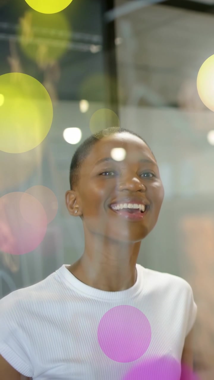 Vertikální video: Modelka reaguje na podnět, usmívá se, otáčí se za sklem, zatímco se v reklamě vznáší barevné bokeh