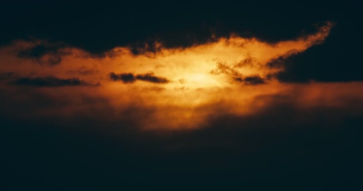 Dark storm clouds illuminated by golden sunset light. Dramatic glowing cloud formations create a moody atmospheric evening sky and striking weather scene.