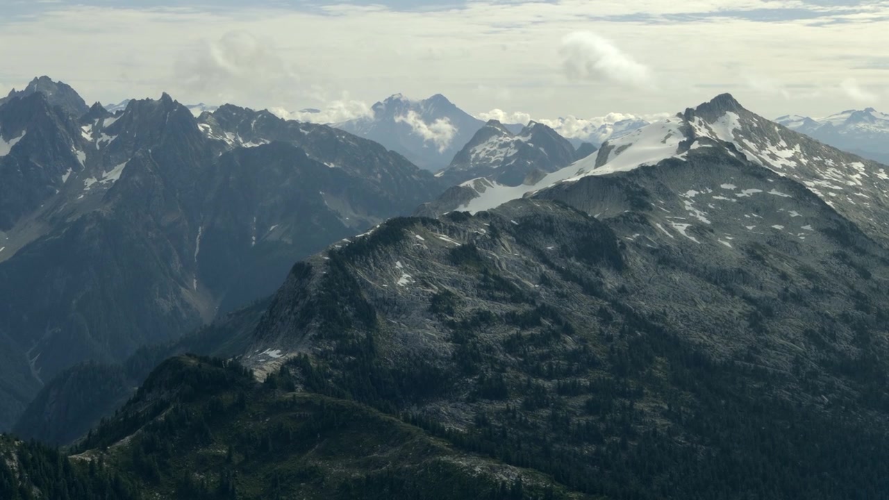 Steep Mountain Range With Rugged Exposed Rock Faces And Scattered Patches Of Snow. Aerial Shot