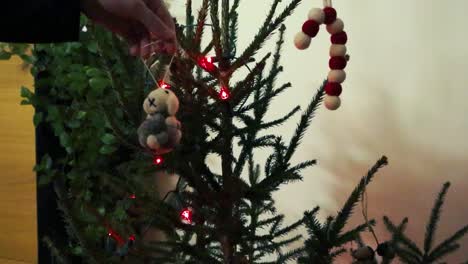 lentamente en movimiento imágenes de una mano femenina colocando una decoración de oveja de fieltro en un árbol de navidad de vacaciones festivas en cámara lenta mientras las luces led rojas están iluminando las agujas y ramas verdes del árbol.