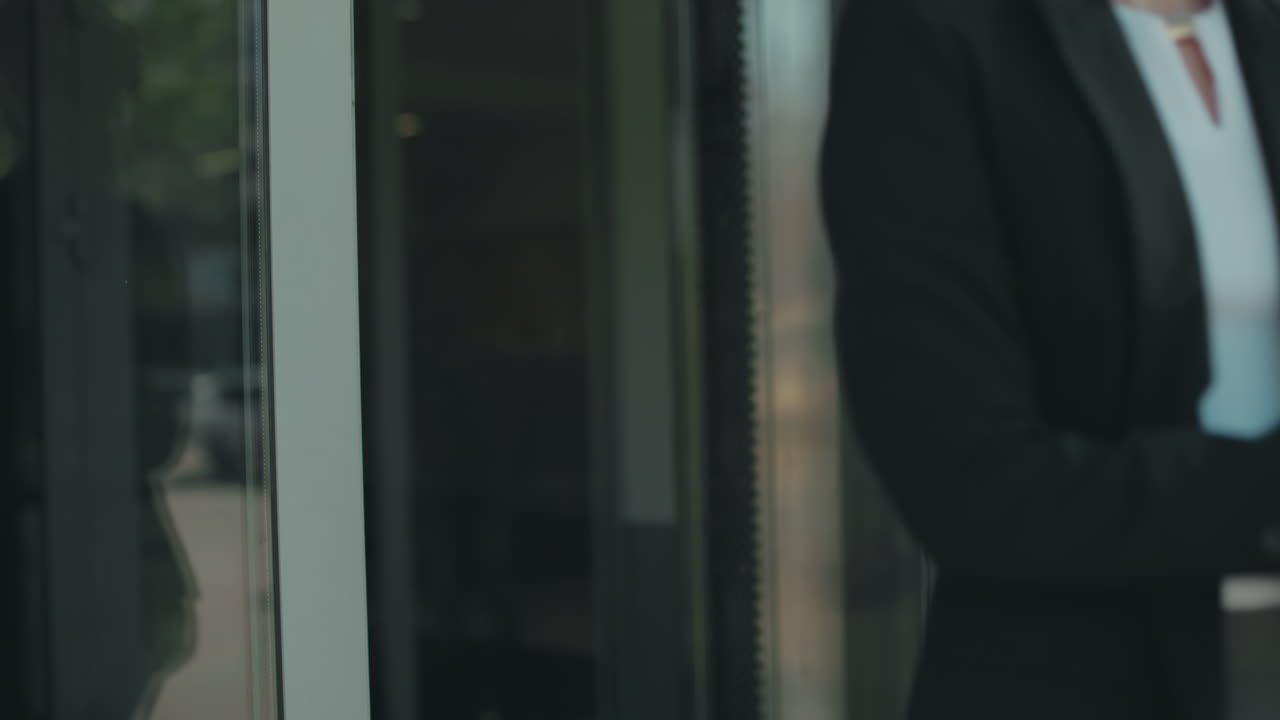 Elegant woman with handbag opening glass door walking out of office building, focus on motion, professionalism, and urban environment with daylight reflections on door