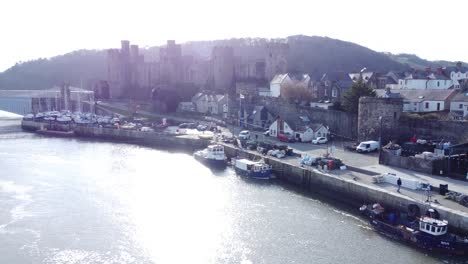 idyllic conwy castle and harbour fishing town boats on coastal waterfront aerial rising backwards reveal