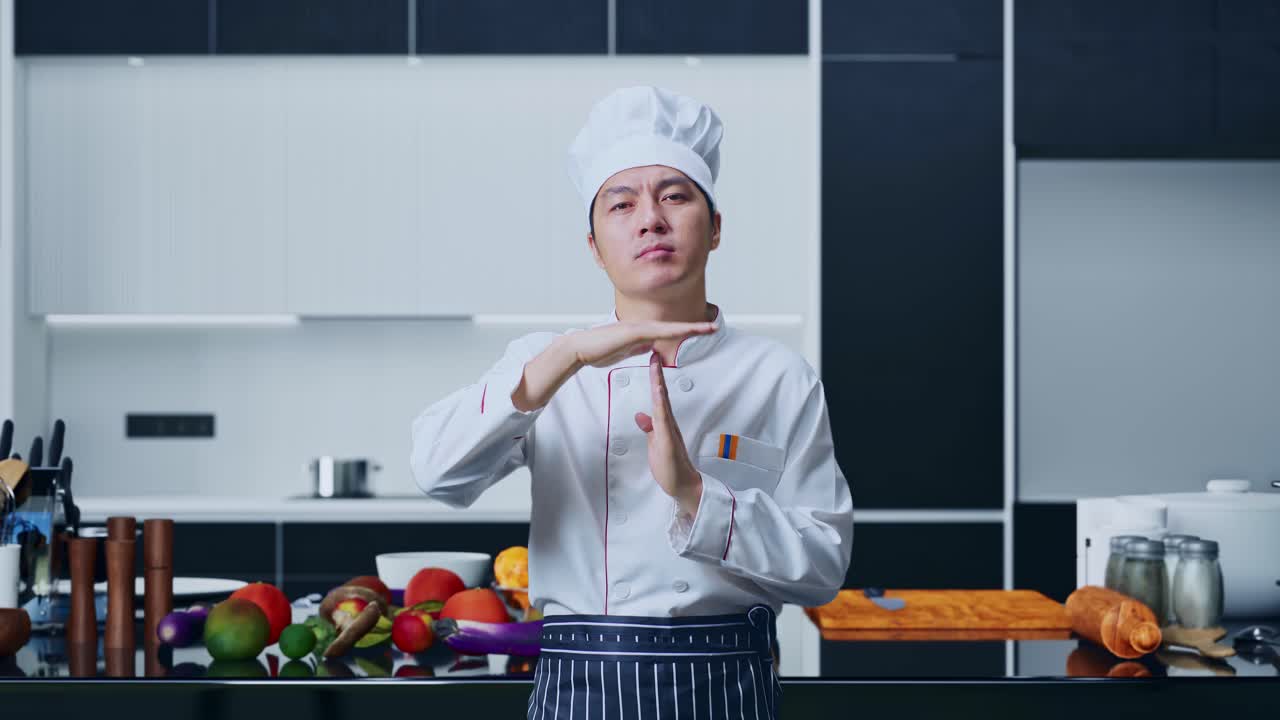 아시아 남자 요리사 는 카메라 를 보고 집 주방 에 서 있는 동안 손 을 휘두르며 시간 을 보여 준다