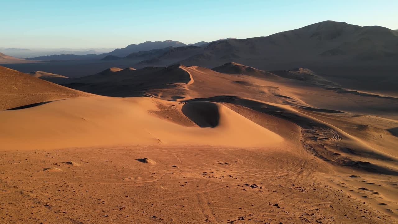 Drone footage soaring above vast desert dunes in Chile’s Atacama, with glowing ridges under a fiery evening sky