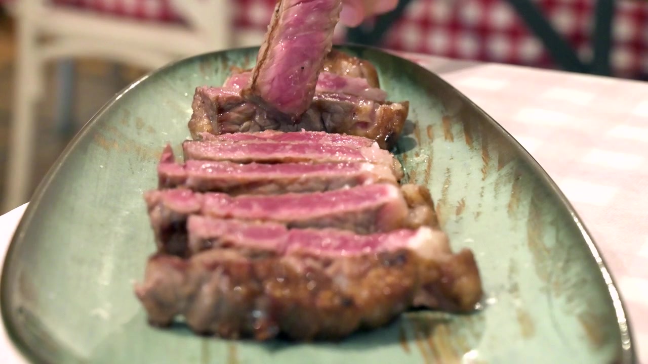 Fettine di bistecca di manzo grigliata su un piatto, prese con una forchetta in un ristorante.