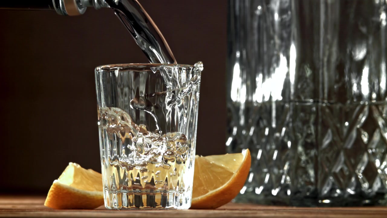 Versamento al rallentatore di un distillato trasparente in un bicchierino da shot con limone