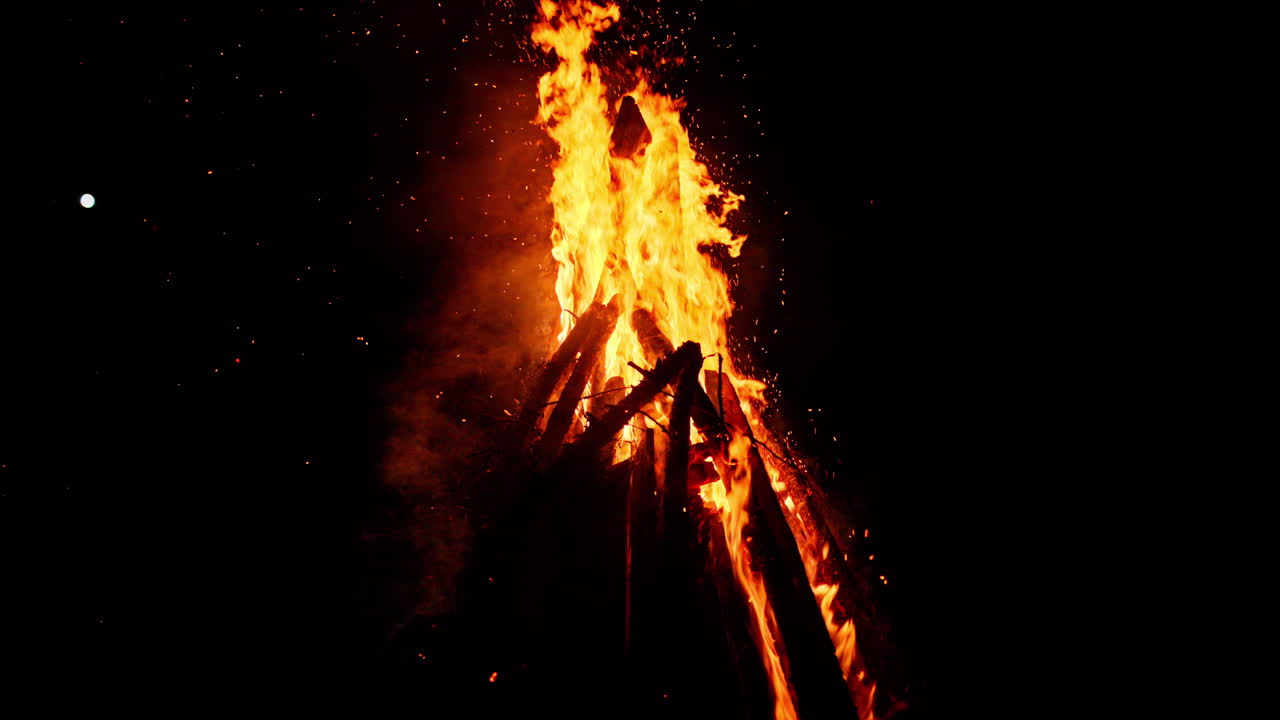 Wood burning in a bonfire at night with a distant view of the mood on the background