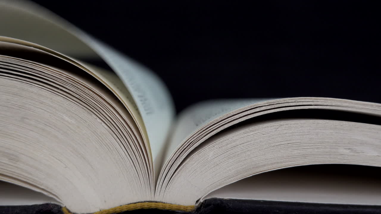 A hand turning the pages of a book lying on a table.