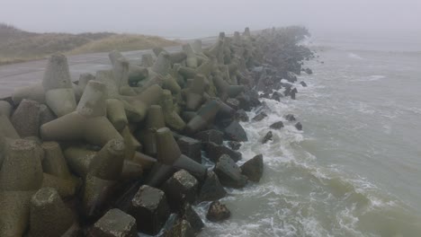 aerial establishing view of port of liepaja concrete pier, baltic sea coastline , foggy day with dense mist, moody feeling, big storm waves splashing, wide ascending drone shot moving forward