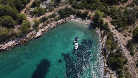 toma de órbita cinematográfica de una playa privada aislada en la isla de brac, croacia, con dos barcos anclados en las aguas turquesas del mar adriático