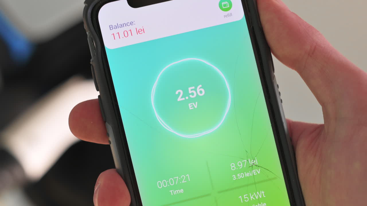 Man charging electro car, holding smartphone with charging process status