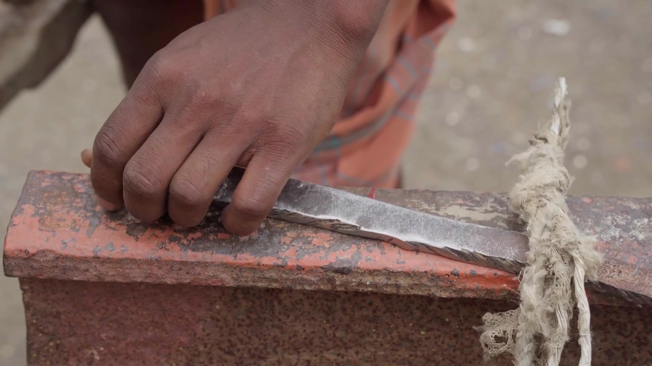Intense close-up video clip of a blacksmith striking metal with a heavy hammer on an anvil. Captures raw manual labor and traditional tool forging at a riverside shipyard in Bangladesh.