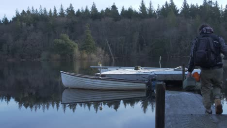 man walks down wooden jetty to set-off in lake boat