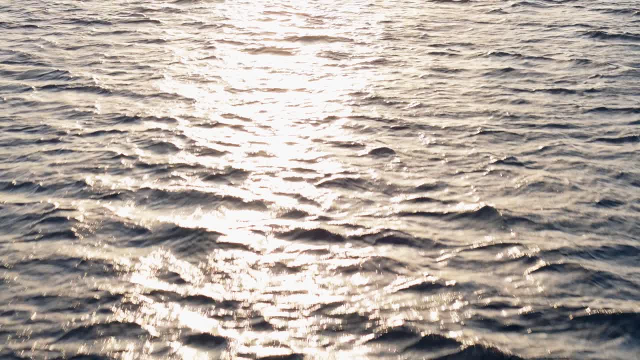 Low flying bird's eye view of sunlight glistening across open ocean at golden hour