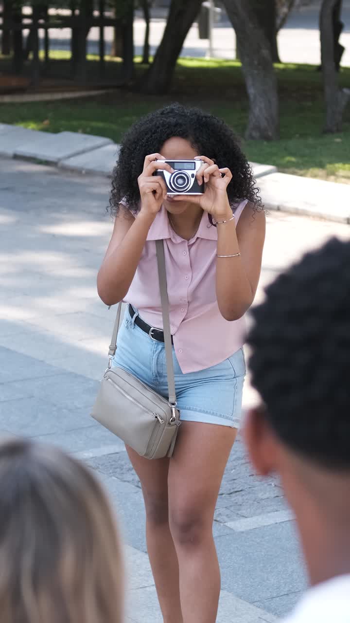 Donna che fotografa amici con una fotocamera digitale in una strada cittadina.