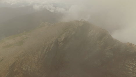 Los-Excursionistas-Llegan-A-La-Cima-De-Una-Montaña-Nublada-Mientras-La-Cámara-Los-Rodea.