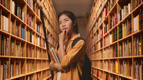 side view of asian woman student with a backpack and some books thinking and looking around while standing in the library