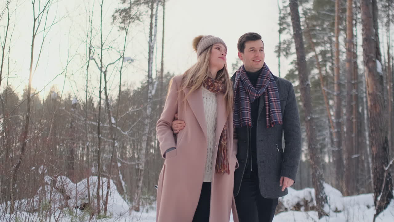 Young married couple in love walking in the winter forest. A man and a woman look at each other laughing and smiling in slow motion. Valentine's Day love story.