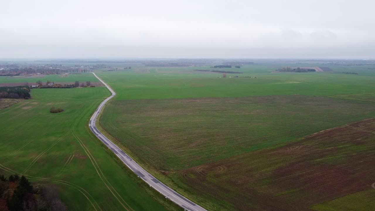 volando sobre las llanuras de lituania con hermosos campos agrícolas verdes y un largo camino solitario