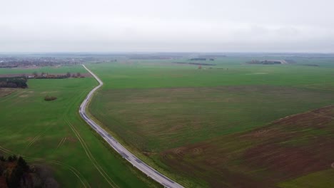 Volando-Sobre-Las-Llanuras-De-Lituania-Con-Hermosos-Campos-Verdes-De-Agricultura-Y-Un-Largo-Camino-Solitario