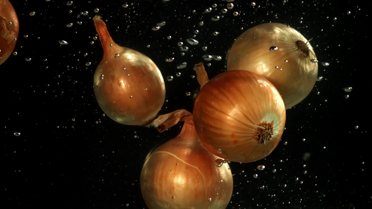 Frische braune Zwiebeln schweben im Wasser mit Blasen auf schwarzem Hintergrund