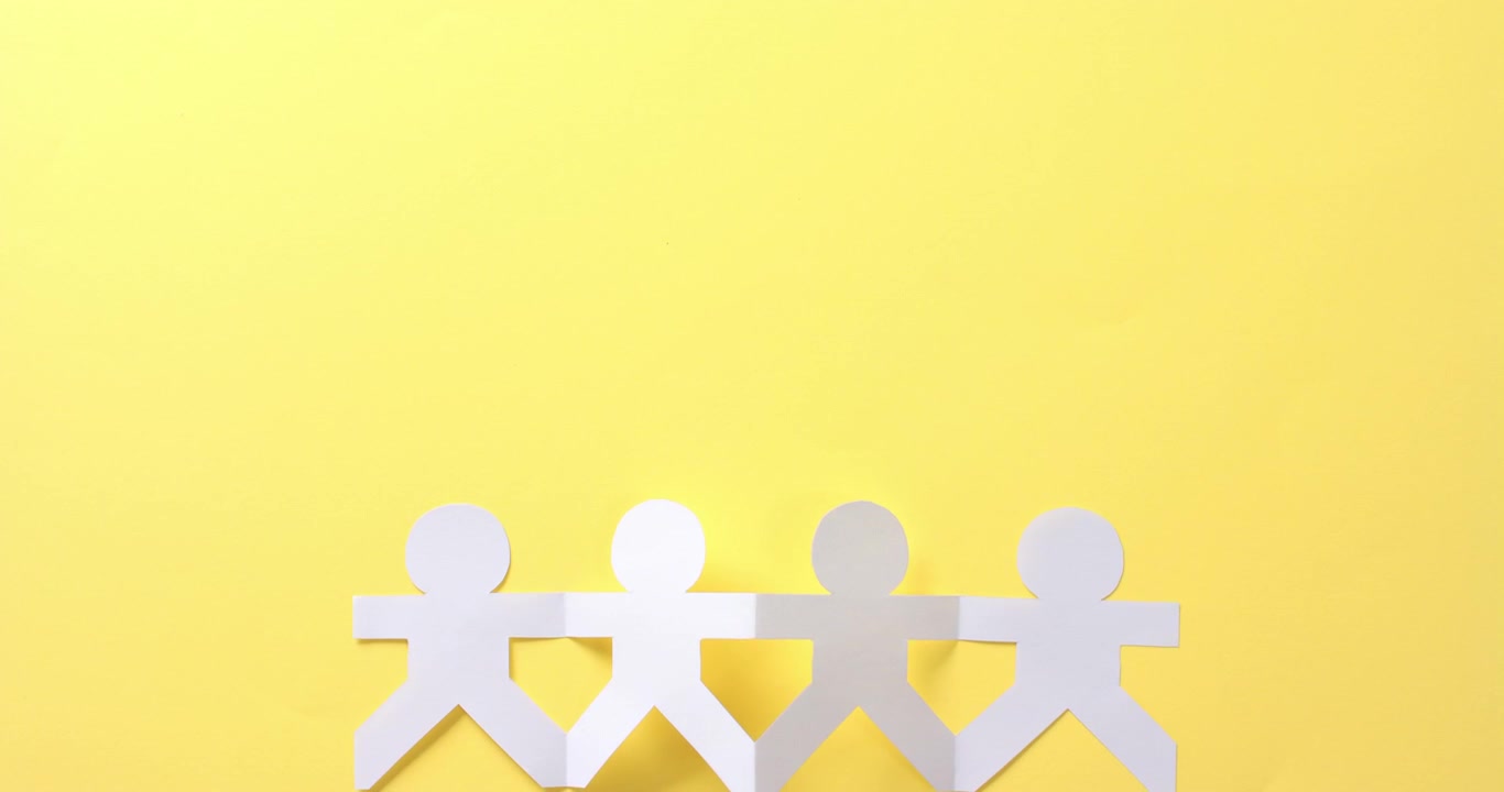 Close up of people holding hands made of white paper on yellow background with copy space