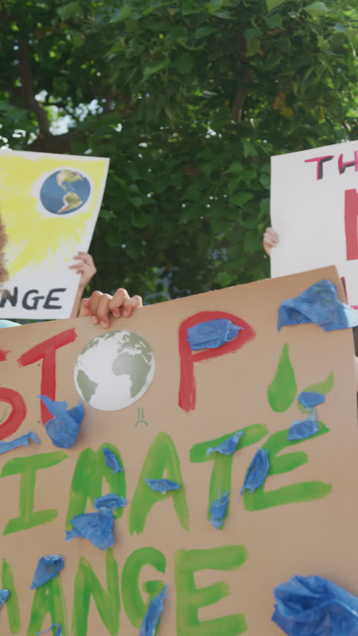 Vertical video of diverse schoolchildren holding banners, protesting outdoors, copy space