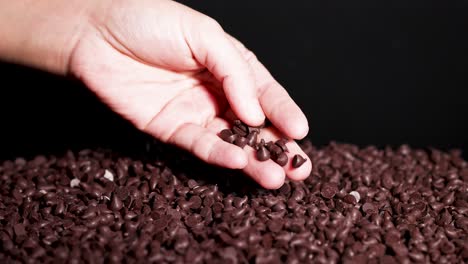 a hand sorts chocolate drops against a dark backdrop, highlighting texture and contrast in a close-up, well-lit setting