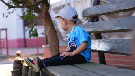 calm caucasian baby boy sitting on the bench in summer. little kid resting outdoors.