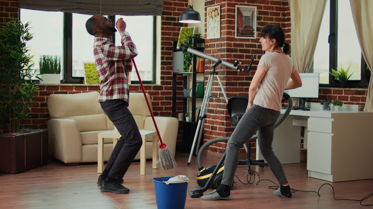 Cheerful people showing dance moves and having fun cleaning living room