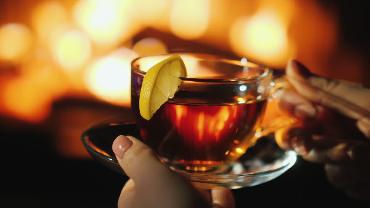 taza con té en manos femeninas junto a la chimenea donde arde el fuego