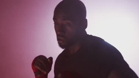 dramatic backlit shot of male boxer in gym wearing wraps on hands training