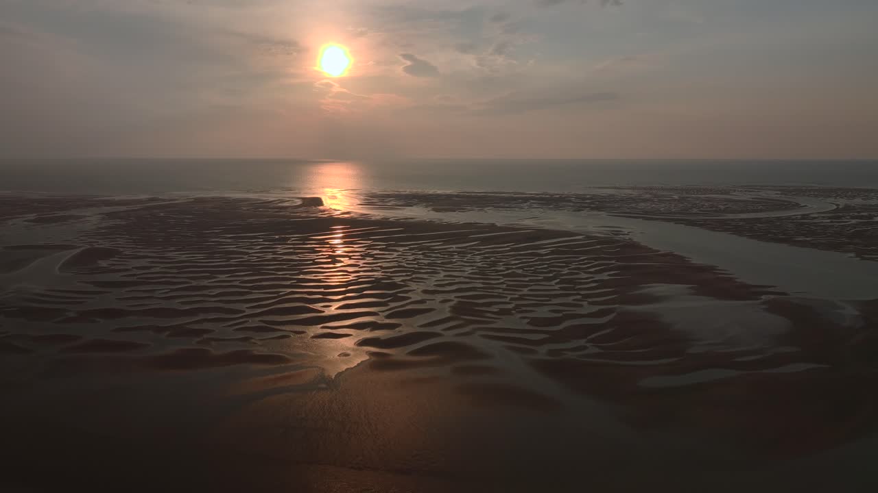 Sunset on sand patterns and pool reflections with sun low on horizon at low tide on coastline. Flight towards sunset. Half speed.