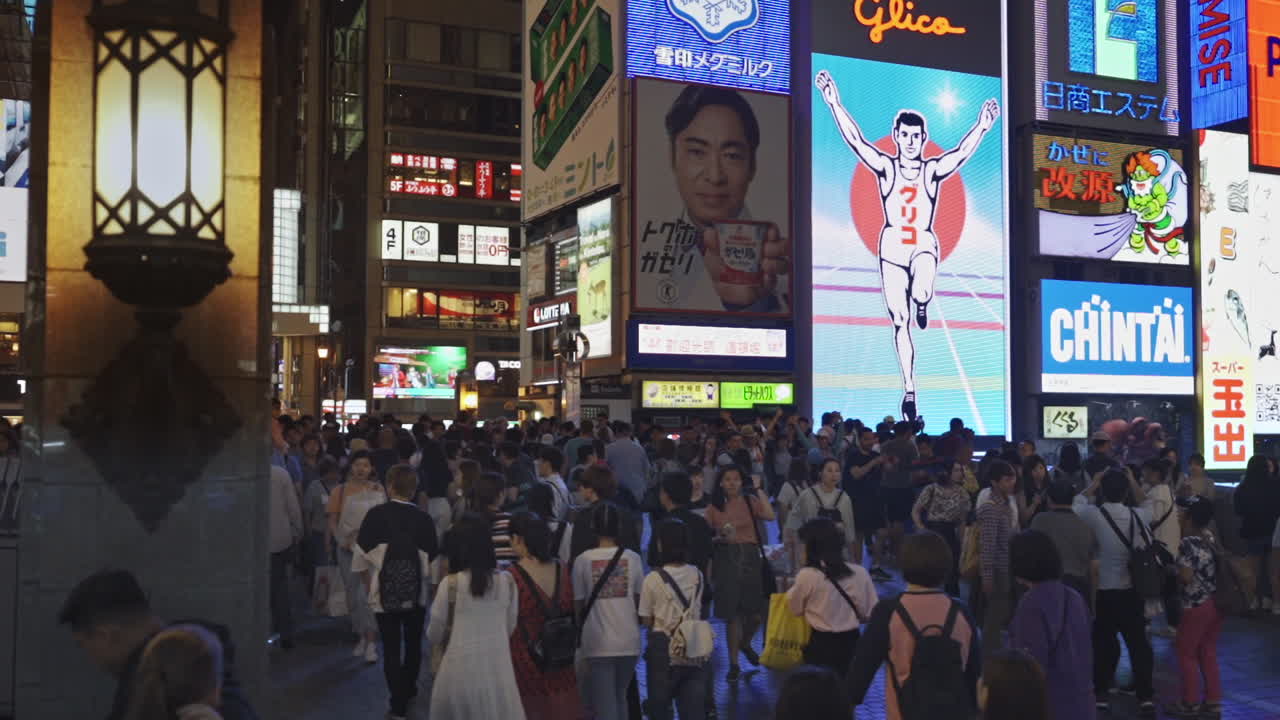 Dotonbori area with people surrounded by large illuminated advertisement including the Glico Running Man, Osaka, Japan, wide truck right in slow motion.