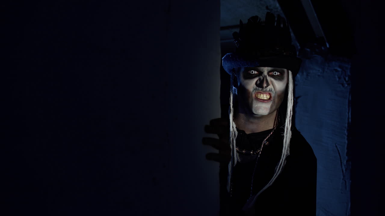 할로윈 스레트 메이크업을 한 악의적인 남자가 어두운 모이에서 울부고 겁을 주려고 나타납니다.