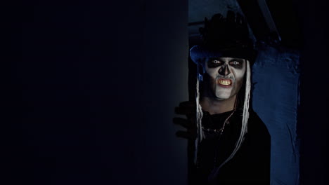 sinister man with halloween skeleton makeup appears from dark corner shouting, trying to scare